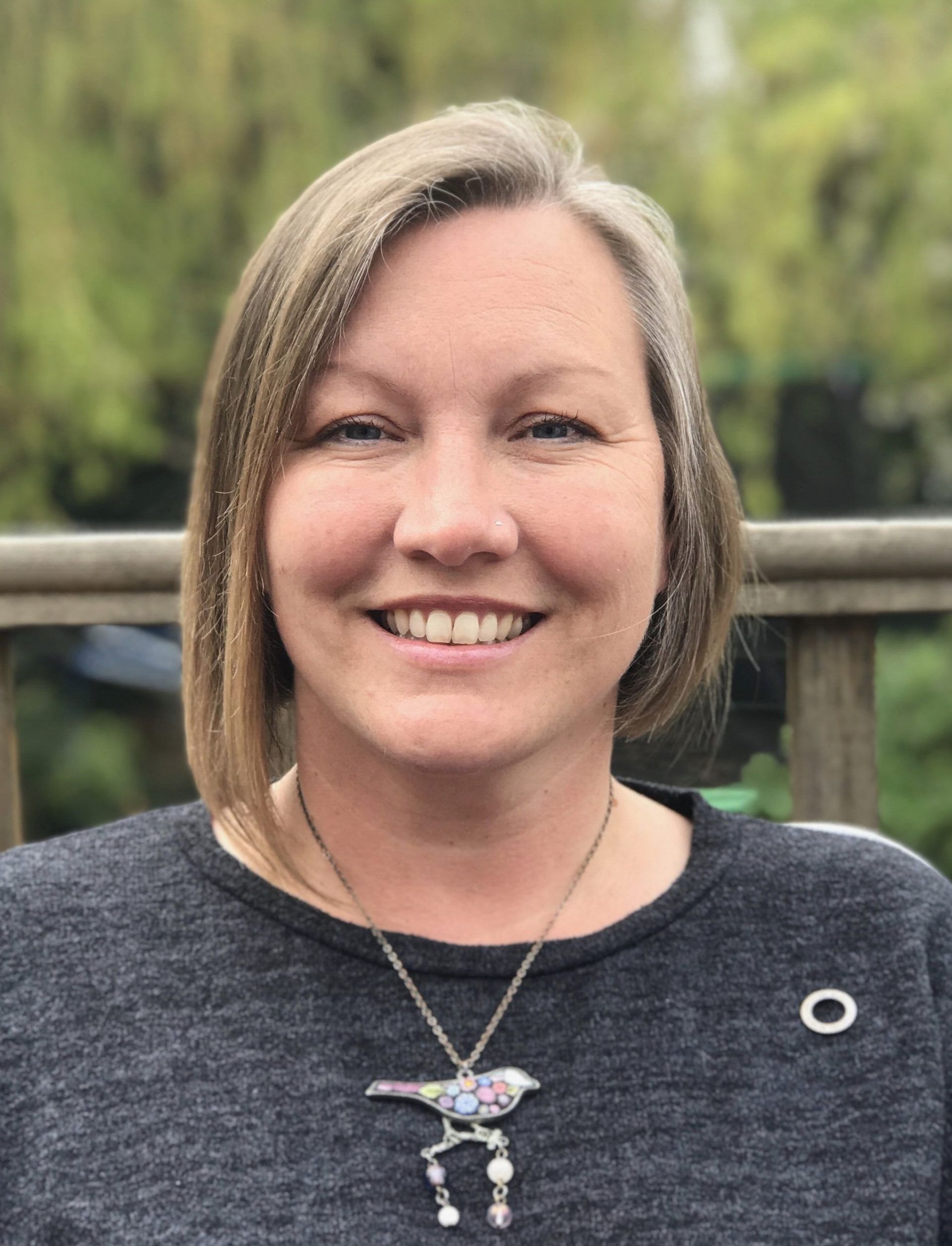 a woman wearing a necklace with a bird on it is smiling for the camera 