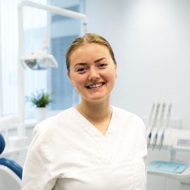 Tannlege Christian med briller og skjegg, iført blå skjorte og medisinsk maske, smiler til kameraet.