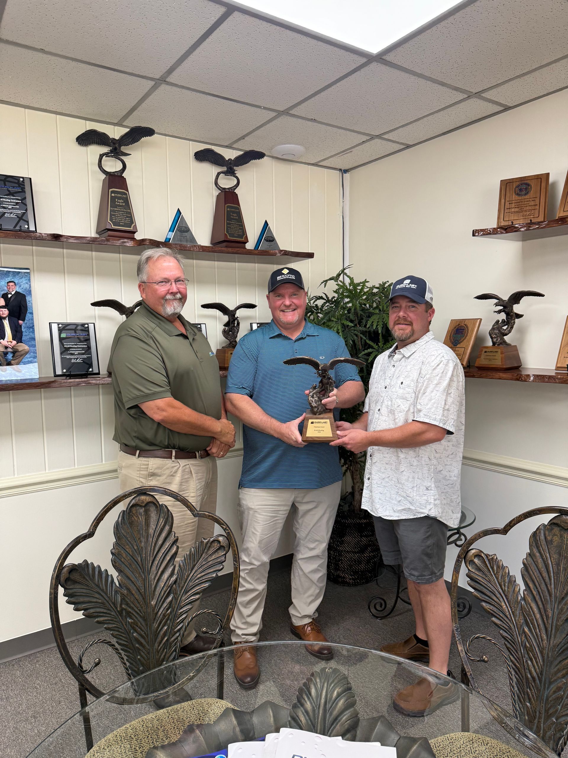 Three people posing indoors with a trophy, in a room displaying large metal sculptures and decor.