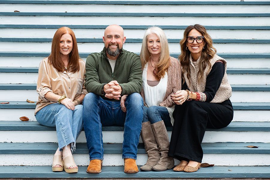 Four people sit on outdoor steps, smiling at the camera in casual clothes.