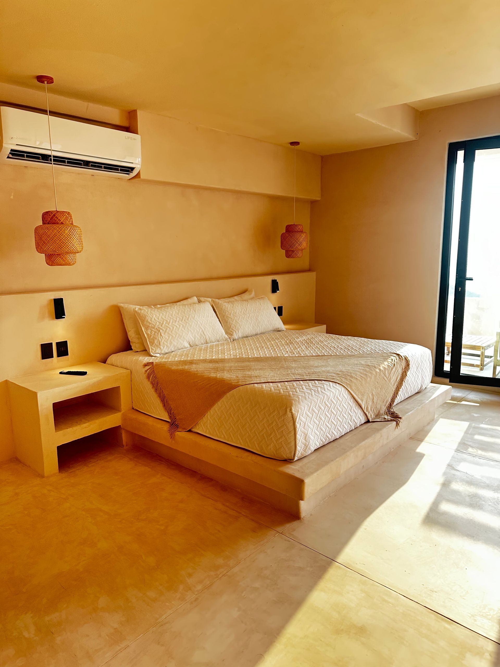Habitación de color beige cálido con una cama bien hecha, mesita de noche, lámparas de pared