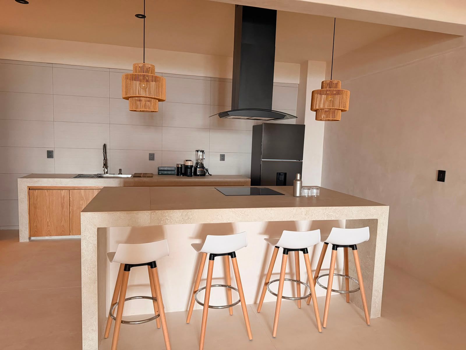 Cocina moderna con isla, cuatro taburetes blancos, armarios de madera y campana extractora negra.