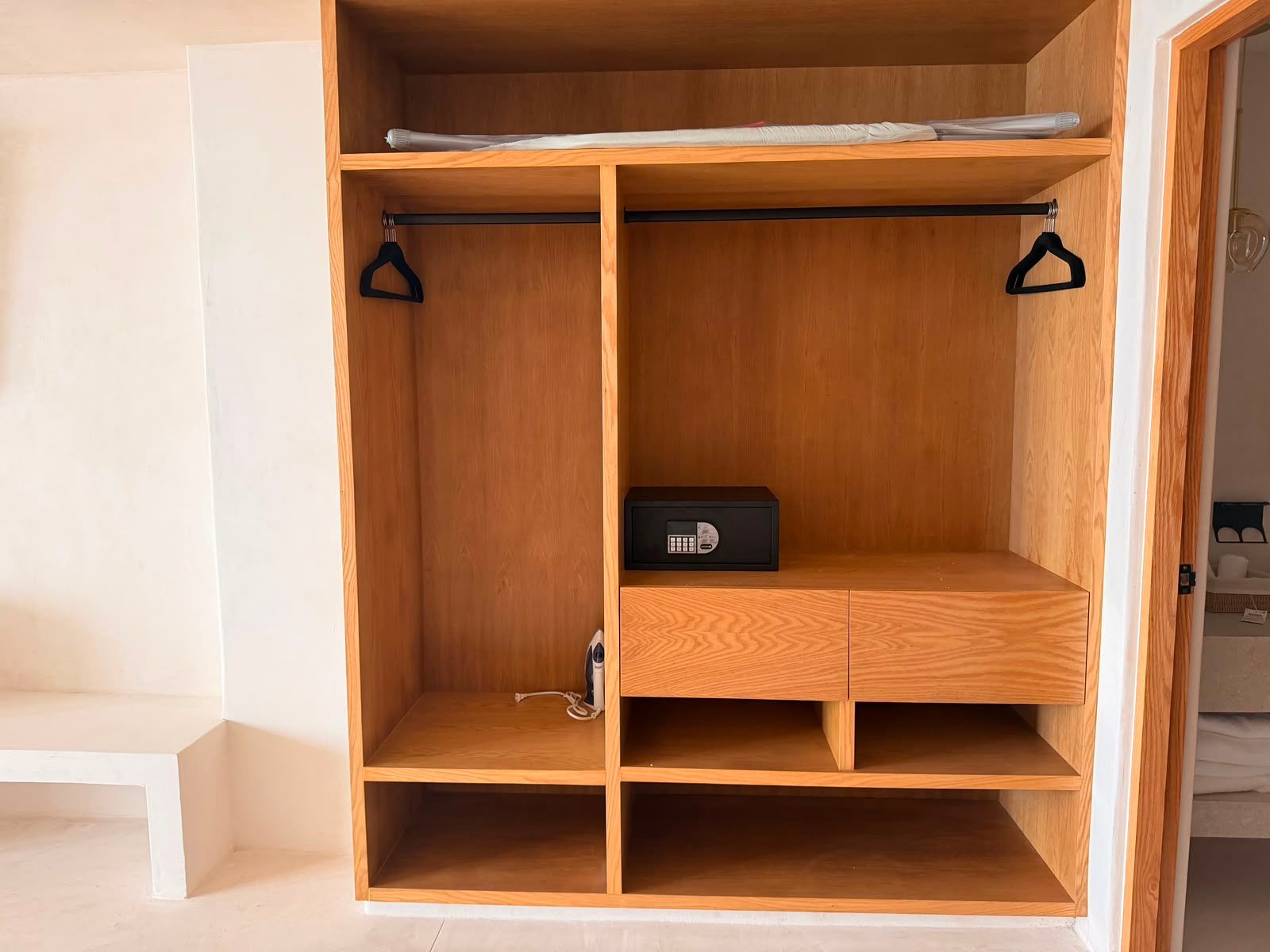 Armario de madera vacío con estantes, cajones y barras para colgar ropa, empotrado en un hueco de la pared.