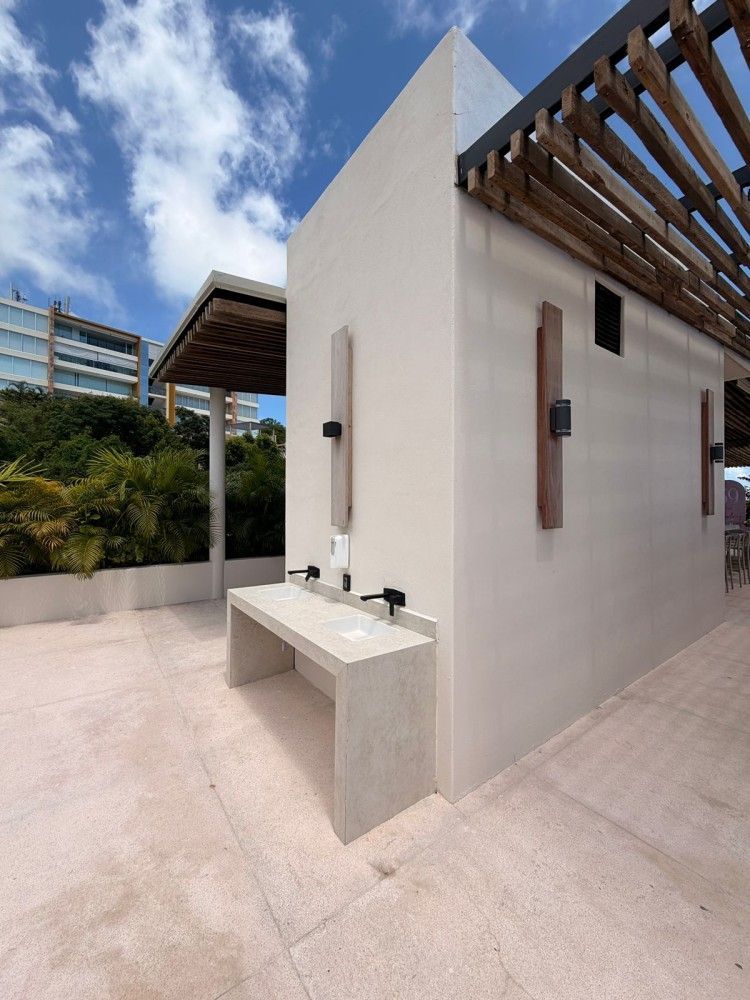 Ducha exterior moderna y banco junto a una pared blanca en una terraza soleada.