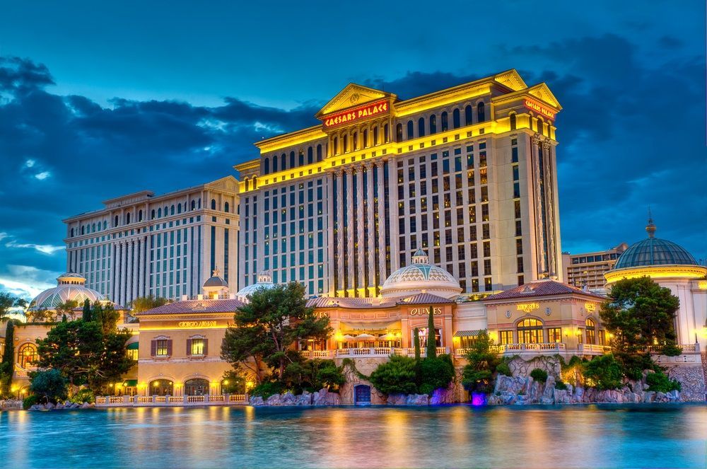 Illuminated luxury hotel and casino at dusk reflected in calm water under a blue sky