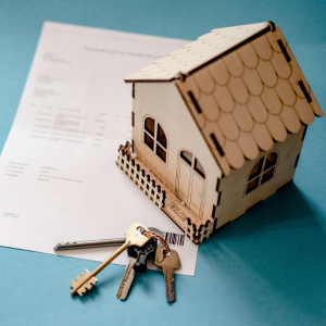 Small wooden house model with keys on a document, on a blue surface.