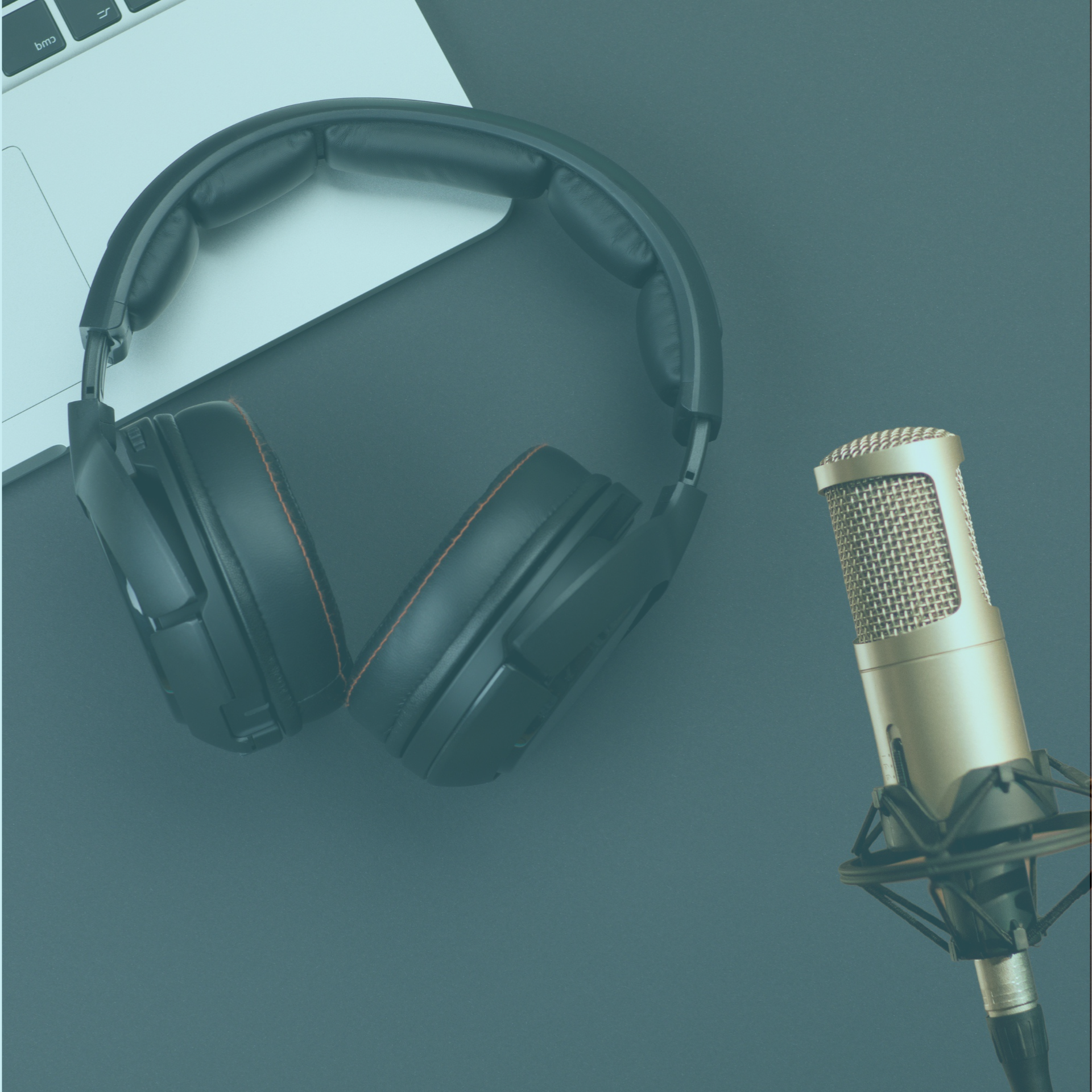 Black headphones and a gold studio microphone on a gray desk with a laptop corner visible