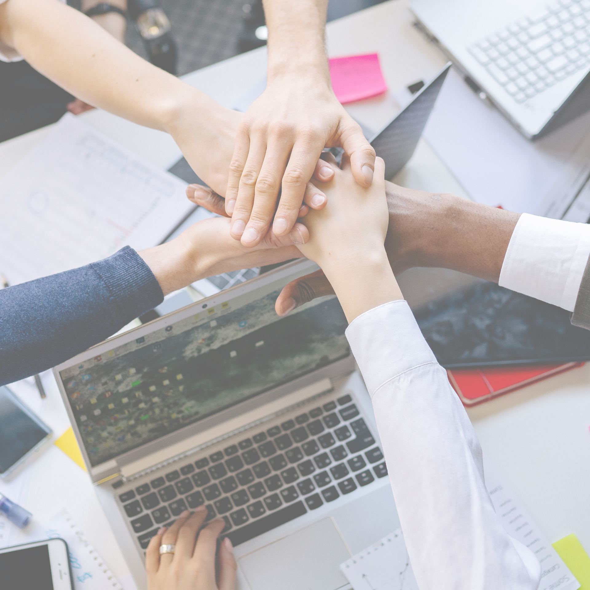 Team hands stacked over laptops in a collaborative office meeting