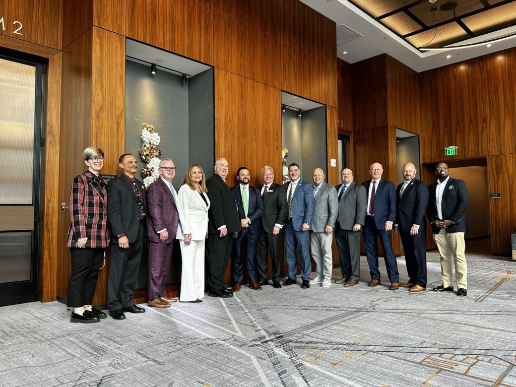 Group of people posing for a photo in a wood-paneled hall with a marble floor.