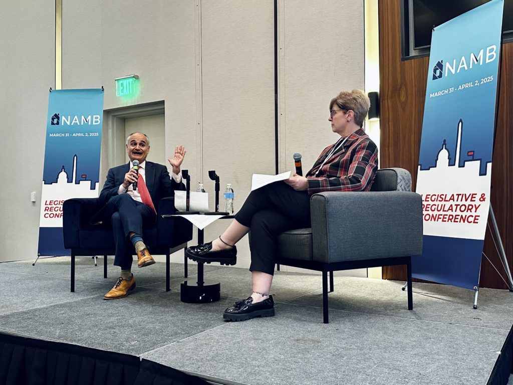Two speakers seated on stage in armchairs during a panel discussion, with event banners behind them.