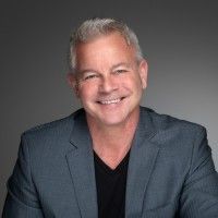 Lauren Patterson Smiling man in a gray blazer and black shirt against a gray studio background