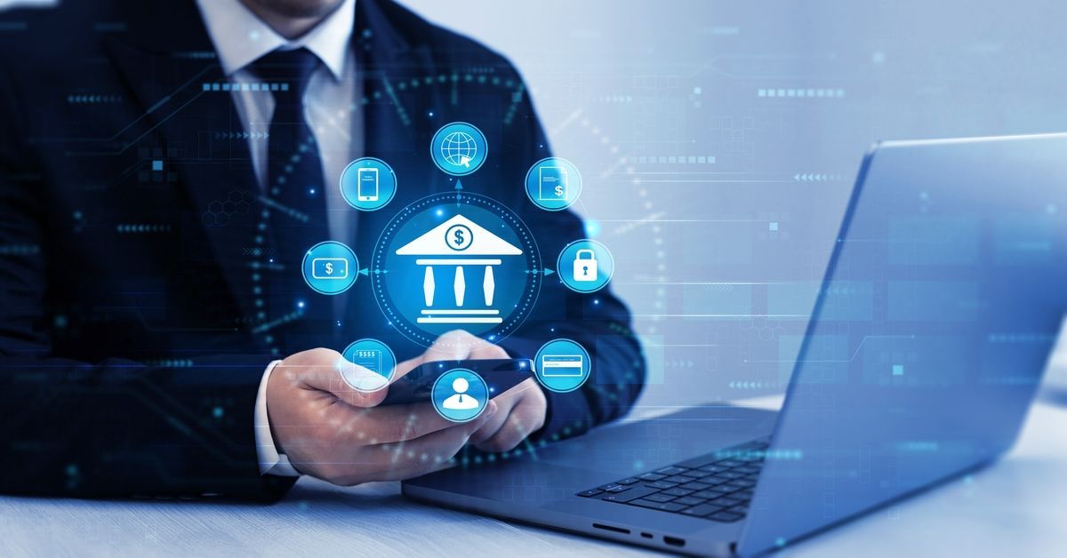 Businessman holding a glowing bank icon beside a laptop, representing digital banking.