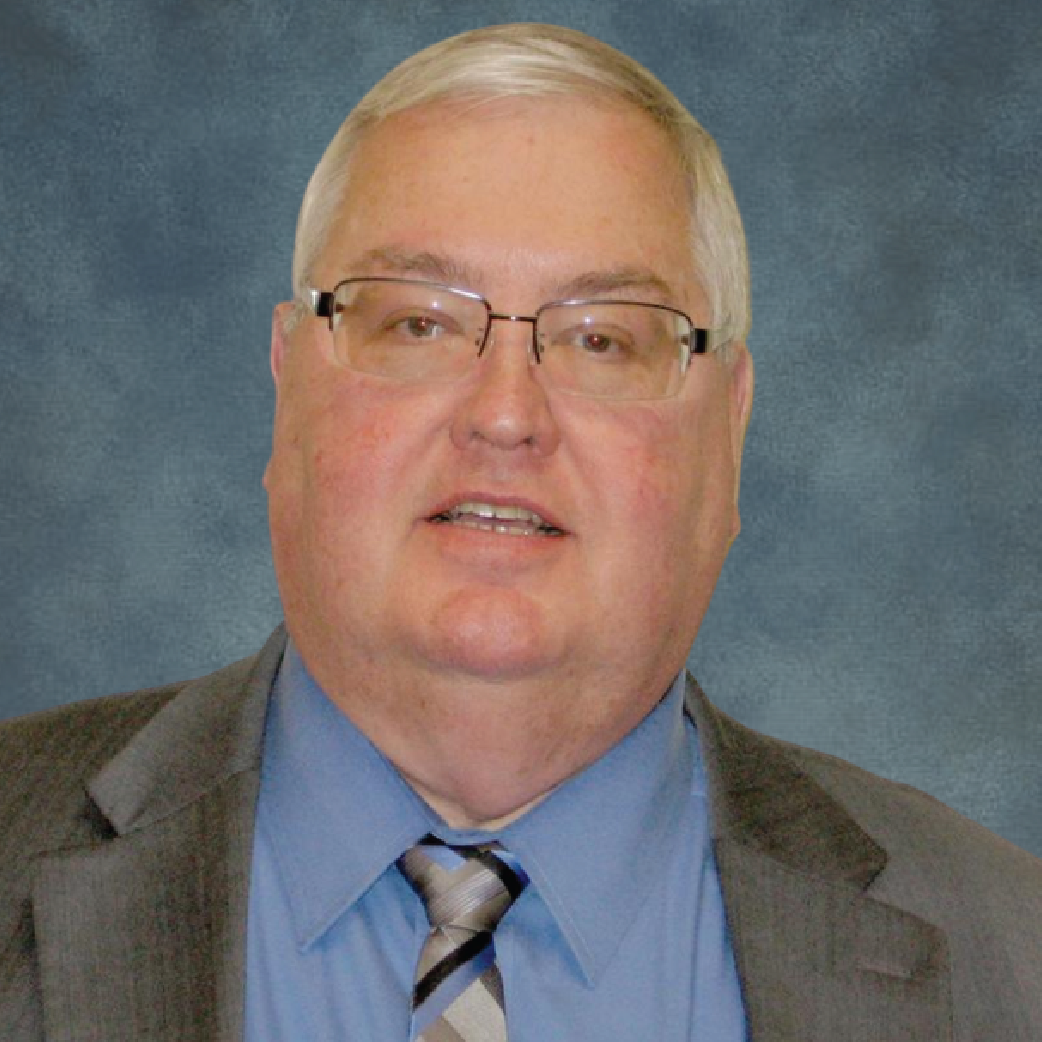 jim-web Studio portrait of a man in a gray suit, blue shirt, and striped tie on a blue-gray backdrop