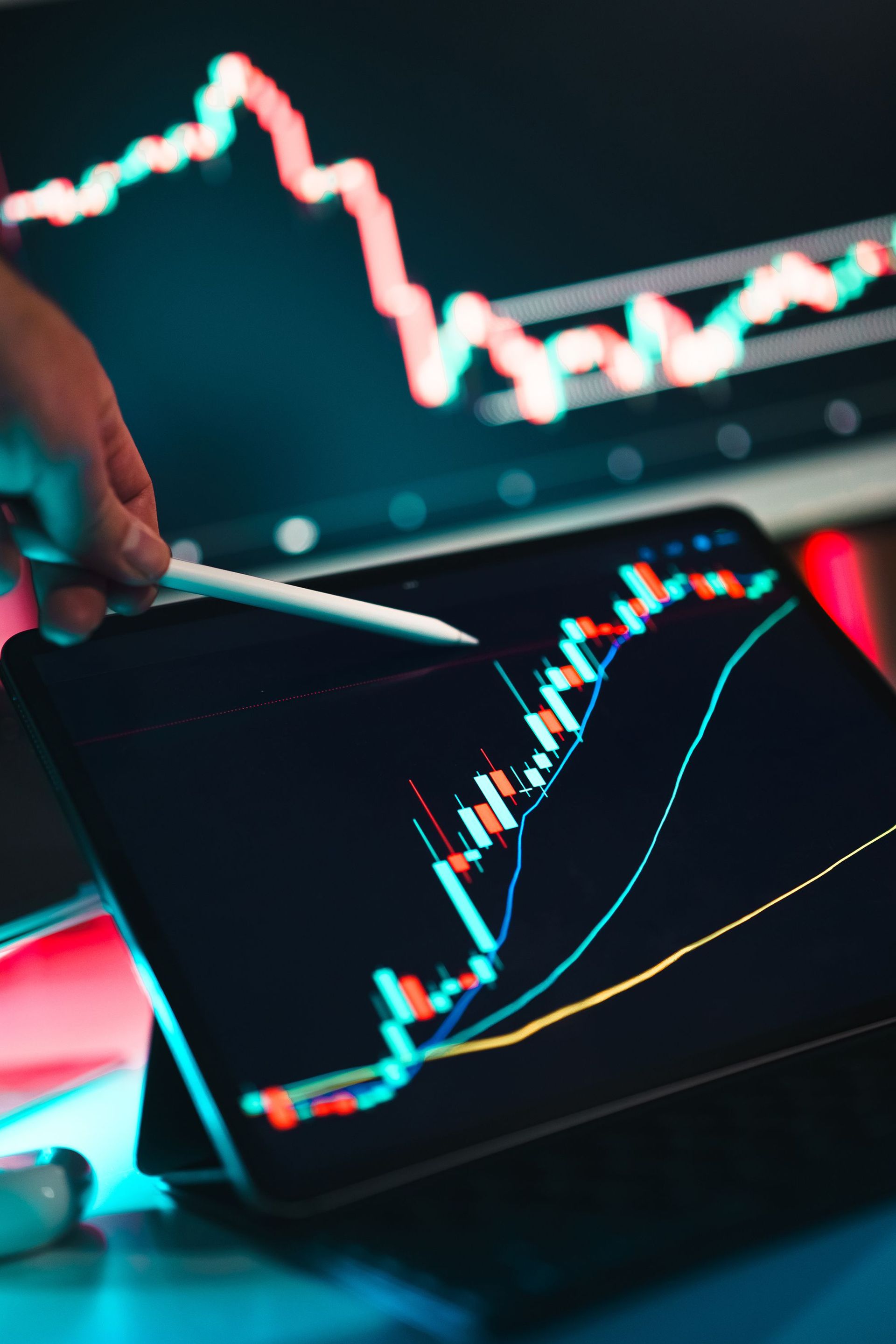 Hand holding stylus over tablet with colorful stock market charts and rising line graphs