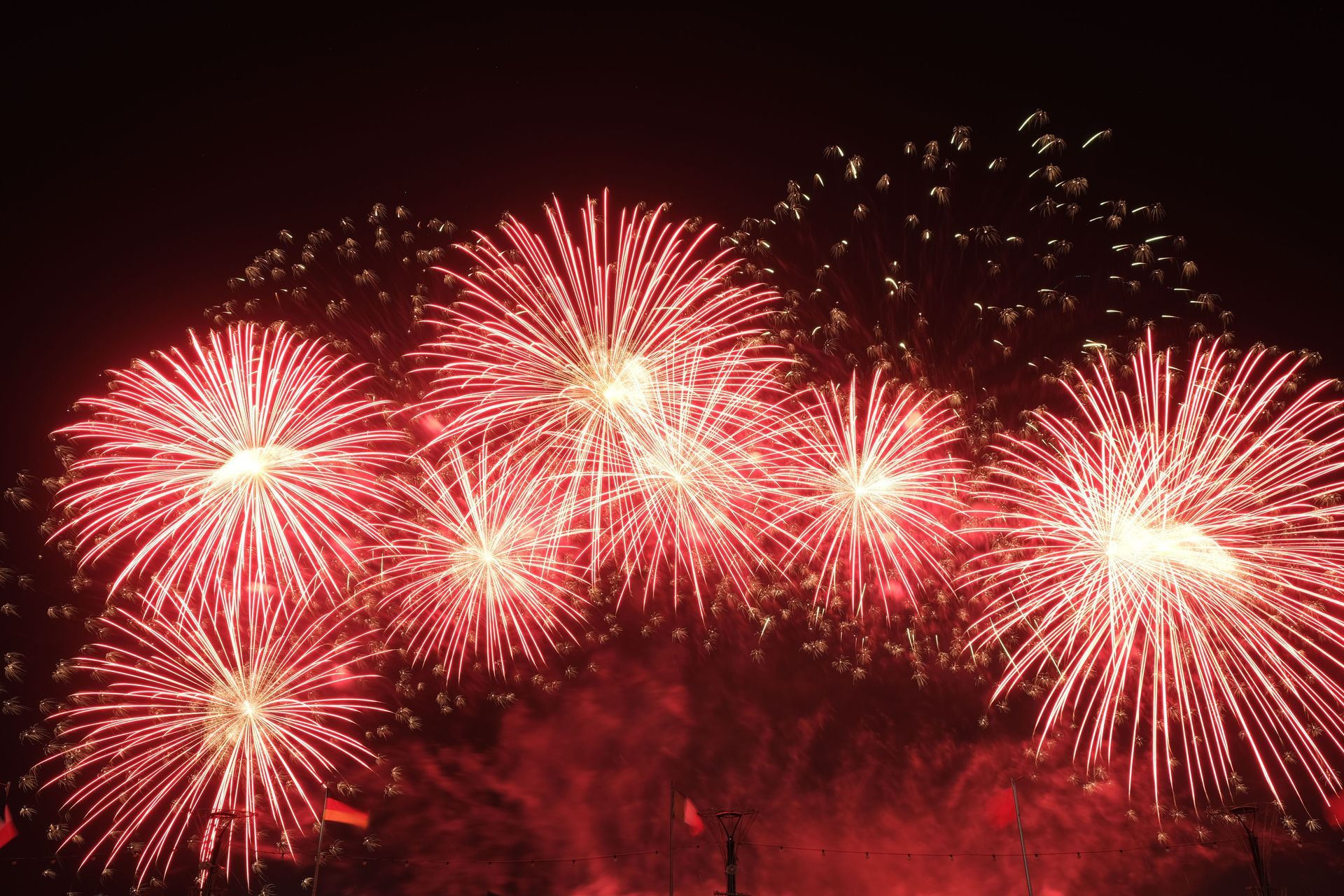 Red fireworks bursting in a dark night sky above a faint crowd silhouette