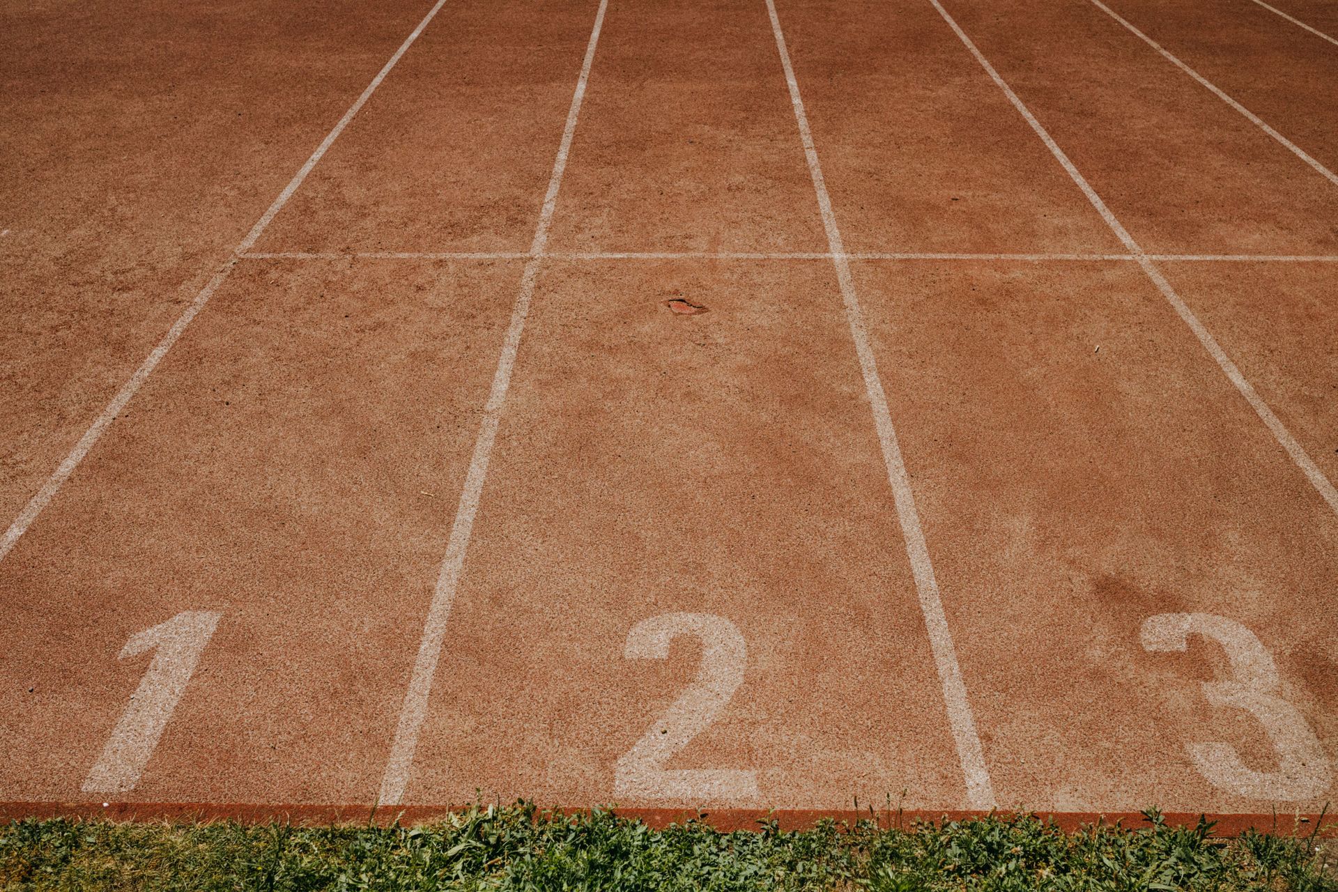 Numbered running lanes on a tan track with white lane lines and green grass at the bottom.