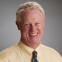 rocke_andrews_200px Smiling man in a pale yellow shirt and colorful tie against a gray background