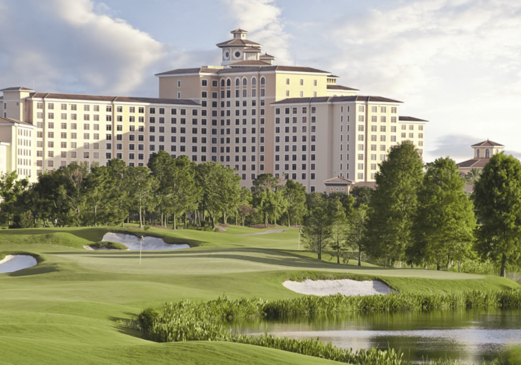 rosen2 Large beige hotel beside a green golf course with ponds and trees under a clear sky