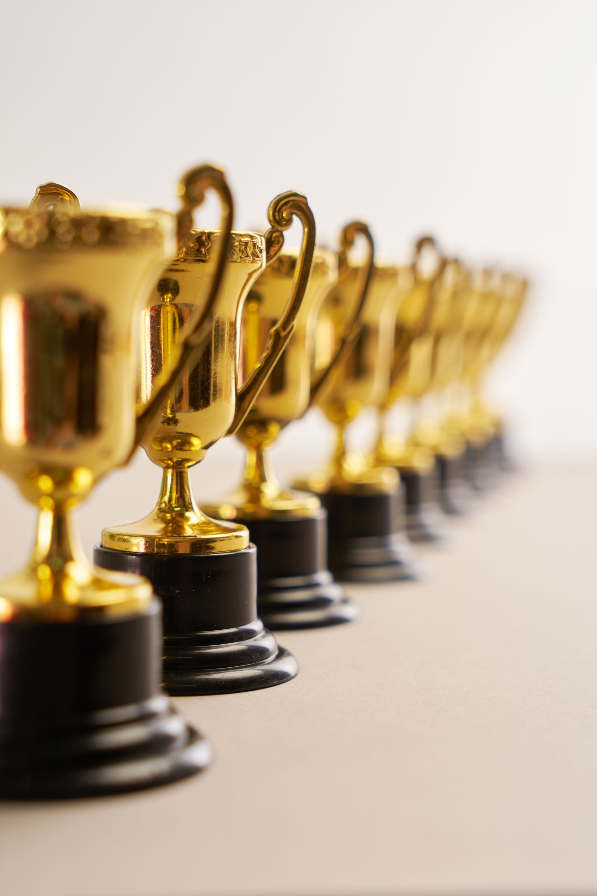 Row of gold trophy figurines on black bases, lined up on a light surface