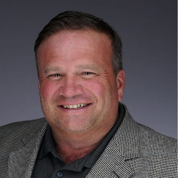 steve-2023-sq Smiling man in a gray blazer against a plain dark background