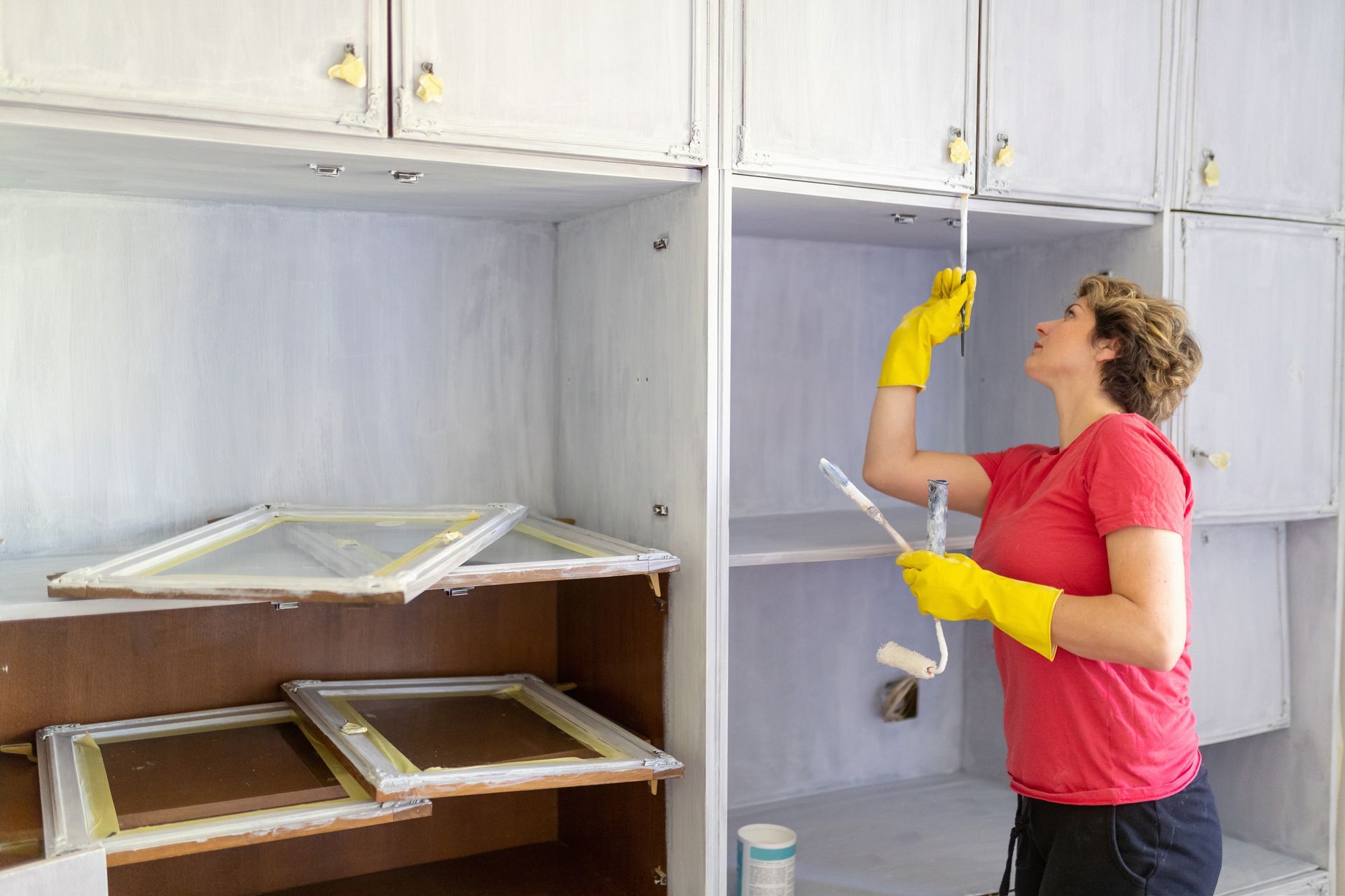 A woman is painting a cabinet with a roller — North Liberty, IA — DeltaPro Painting & Remodeling A woman is painting a cabinet with a roller — North Liberty, IA — DeltaPro Painting & Remodeling