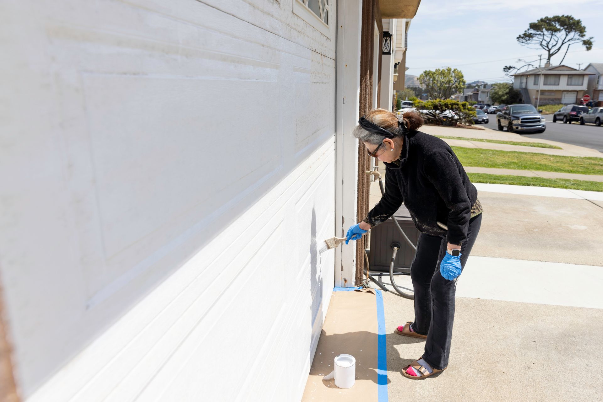A woman is painting a garage door with blue tape — North Liberty, IA — DeltaPro Painting & Remodeling A woman is painting a garage door with blue tape — North Liberty, IA — DeltaPro Painting & Remodeling