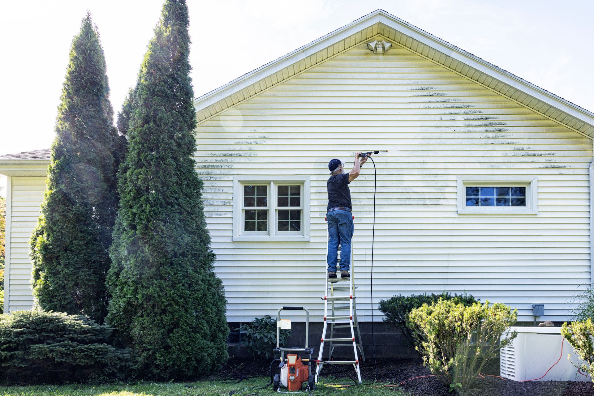 A man is standing on a ladder painting the side of a white house — North Liberty, IA — DeltaPro Painting & Remodeling