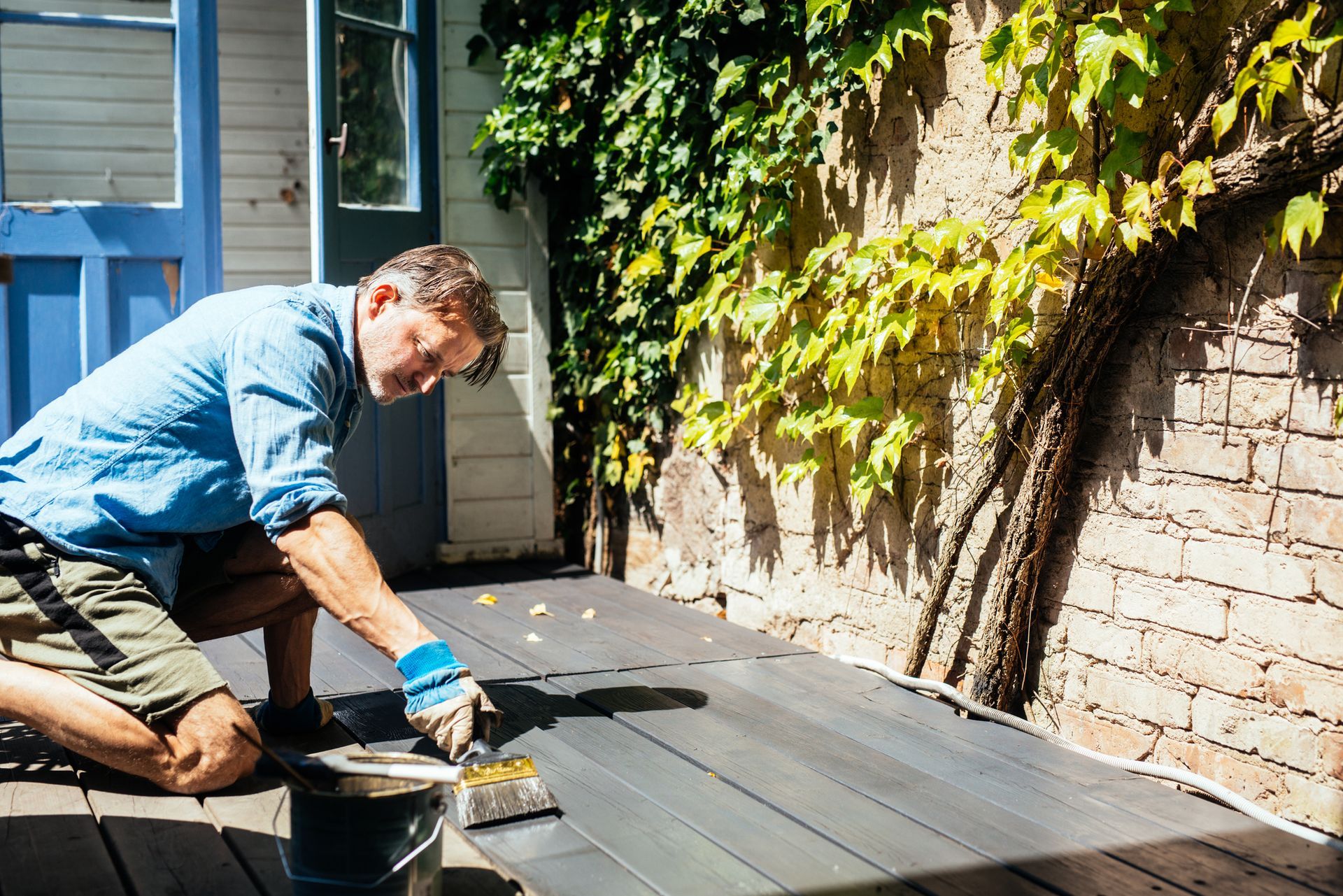 A man is kneeling down and painting a wooden deck — North Liberty, IA — DeltaPro Painting & Remodeling A man is kneeling down and painting a wooden deck — North Liberty, IA — DeltaPro Painting & Remodeling