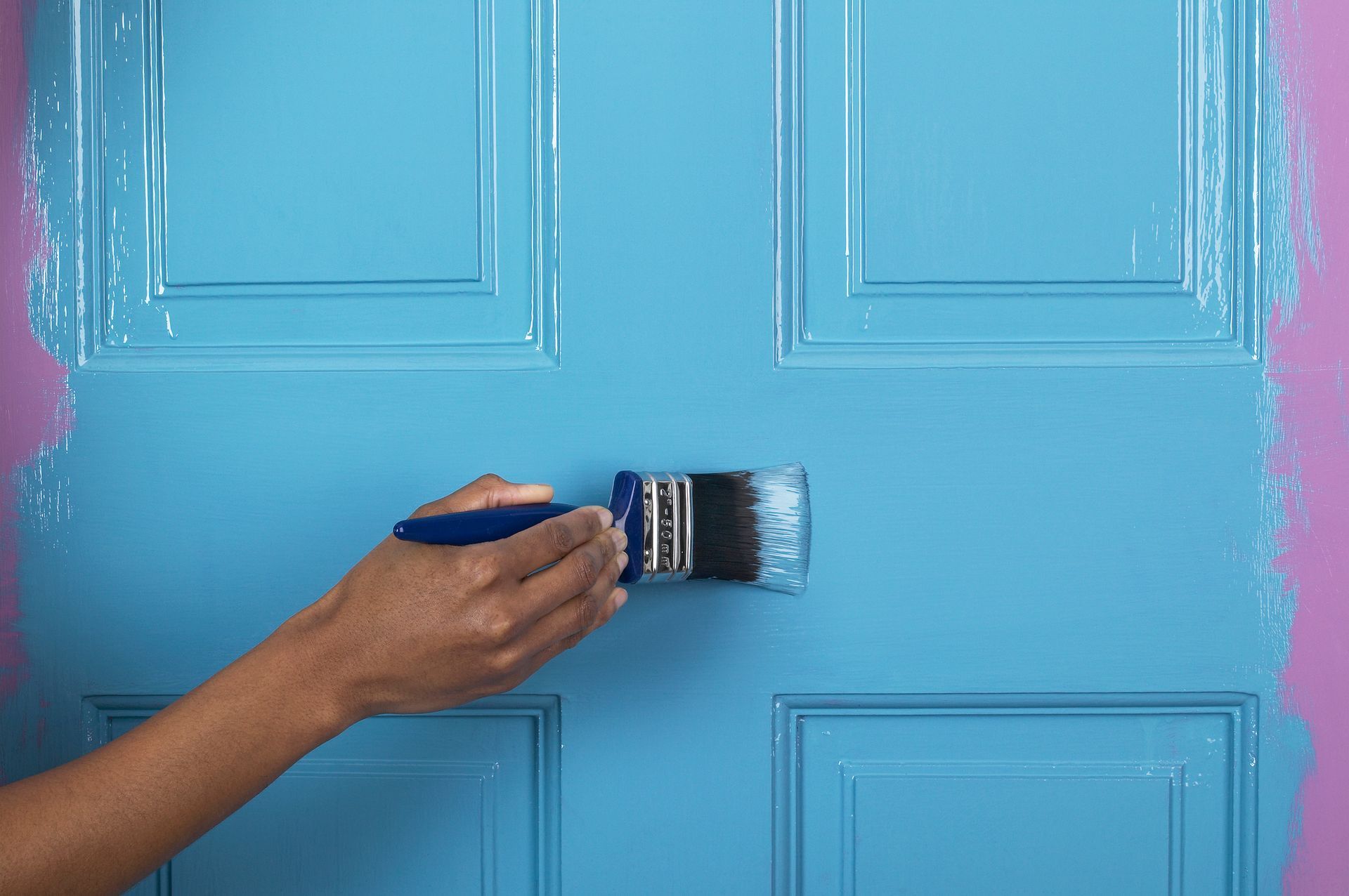 A person is painting a blue door with a brush — North Liberty, IA — DeltaPro Painting & Remodeling A person is painting a blue door with a brush — North Liberty, IA — DeltaPro Painting & Remodeling