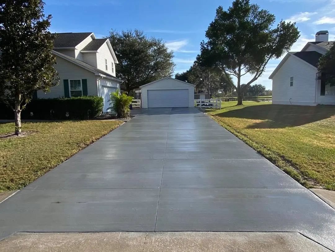 Long concrete driveway leading to a white garage between two houses on a sunny day