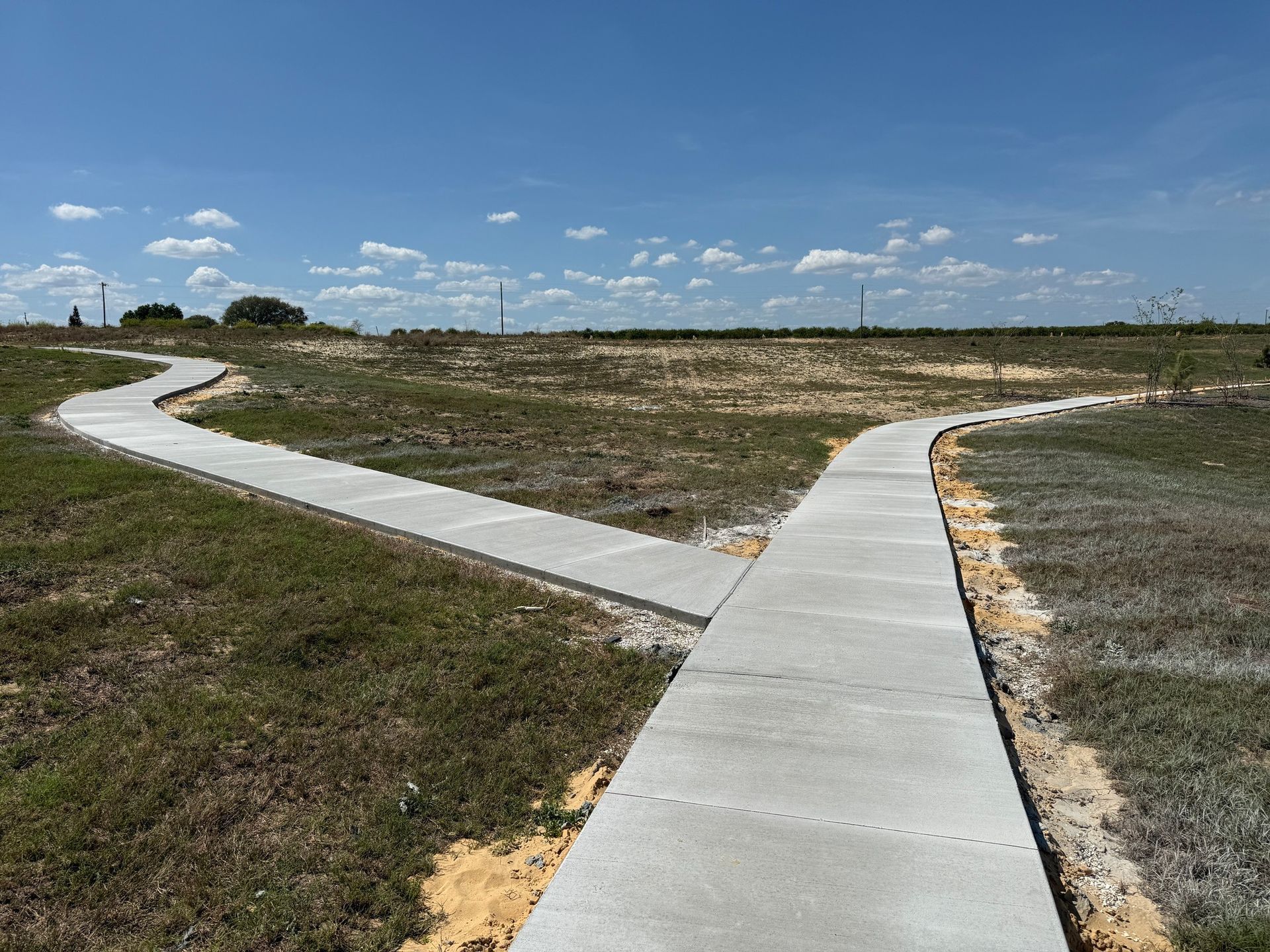 Concrete walkway splits into two paths across a grassy, open landscape under a blue sky.