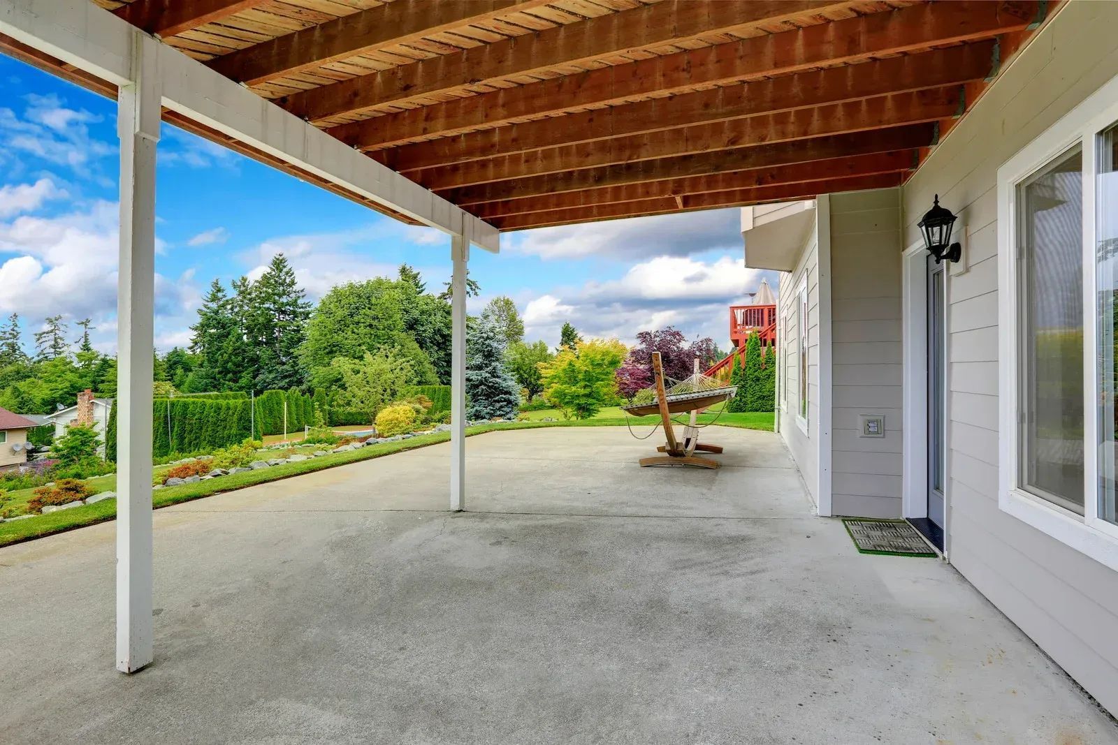 Concrete patio under a covered porch overlooking a lush green yard on a sunny day.