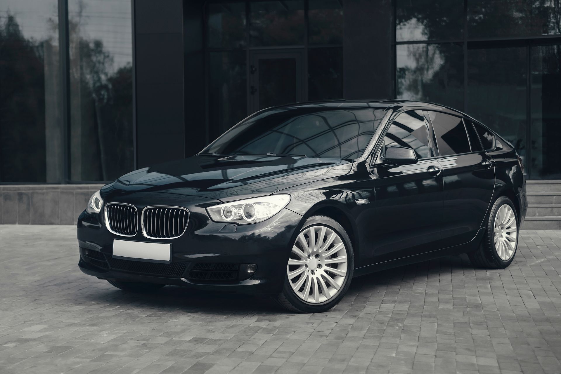 Black sedan parked outside a modern glass building on a paved driveway