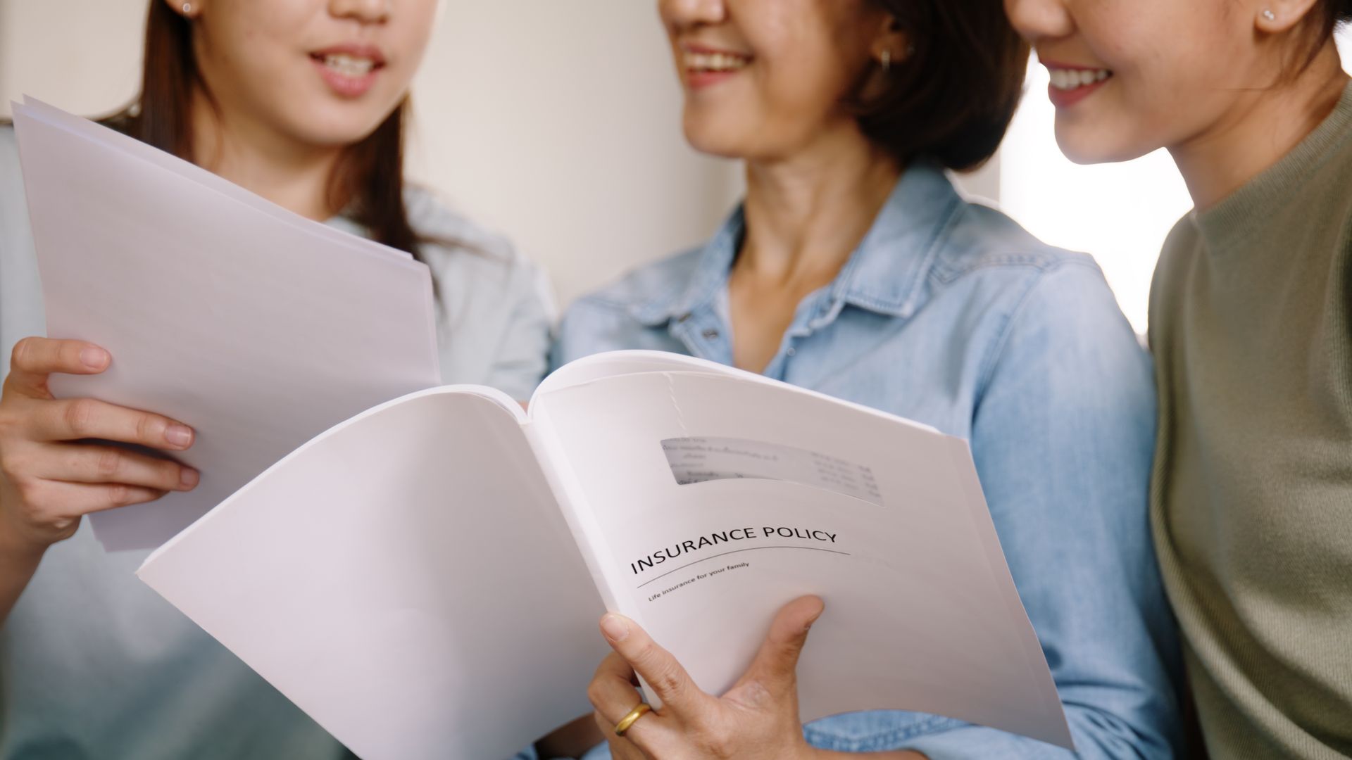 Three people holding and reading open booklets together, smiling in a bright indoor setting