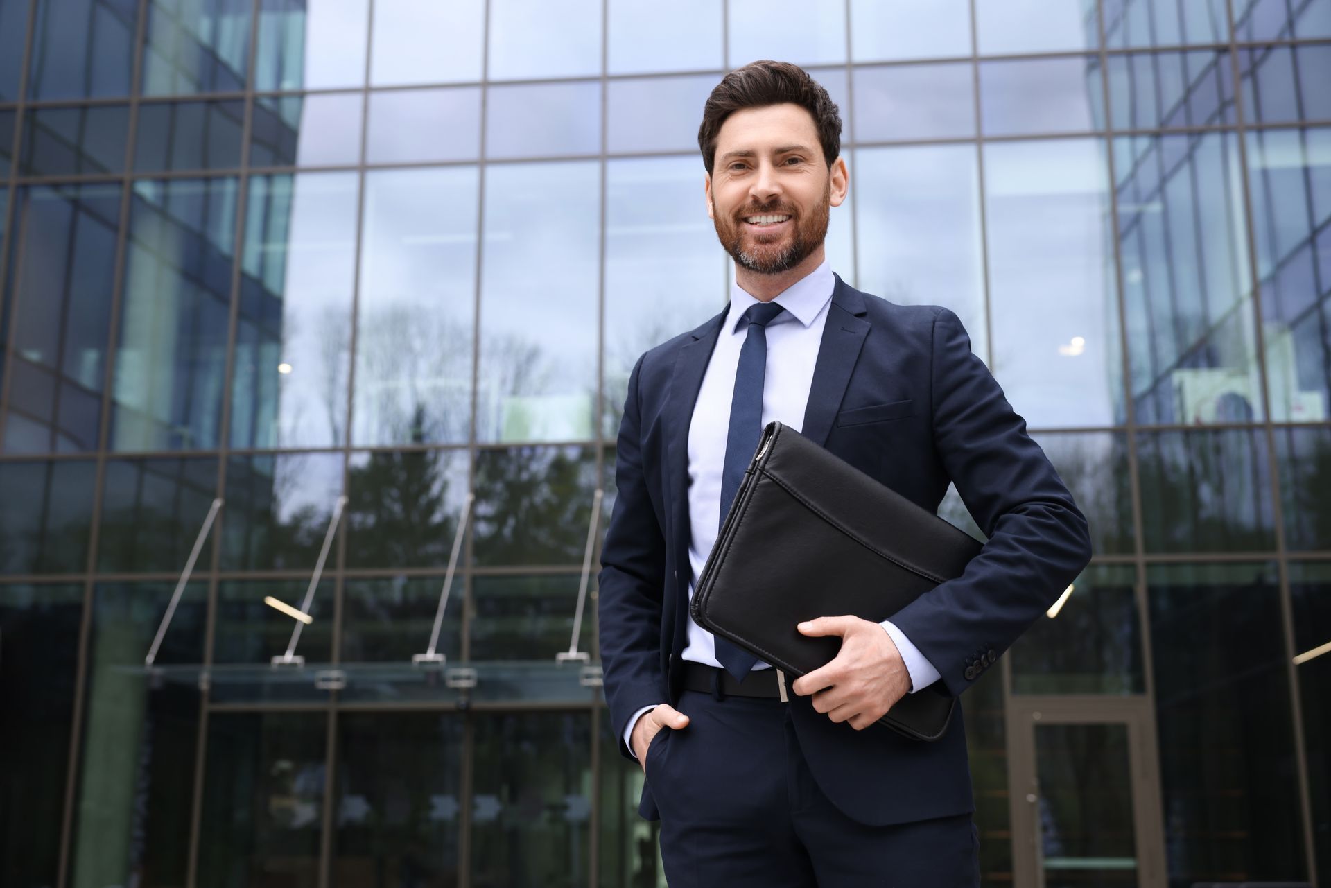 Business professional holding a laptop outside a glass office building