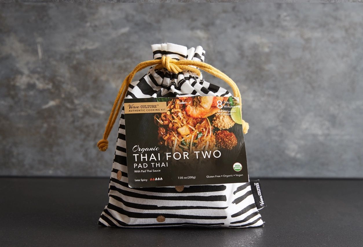 An organic Pad Thai meal kit in a black-and-white striped fabric drawstring bag with a yellow rope handle.