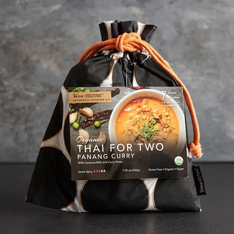 A black drawstring bag with white circles containing a Thai for Two Panang Curry meal kit against a dark grey background.