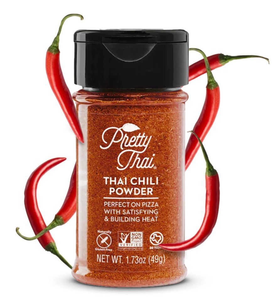 A spice jar of Pretty Thai Thai Chili Powder, surrounded by four red chili peppers on a white background.