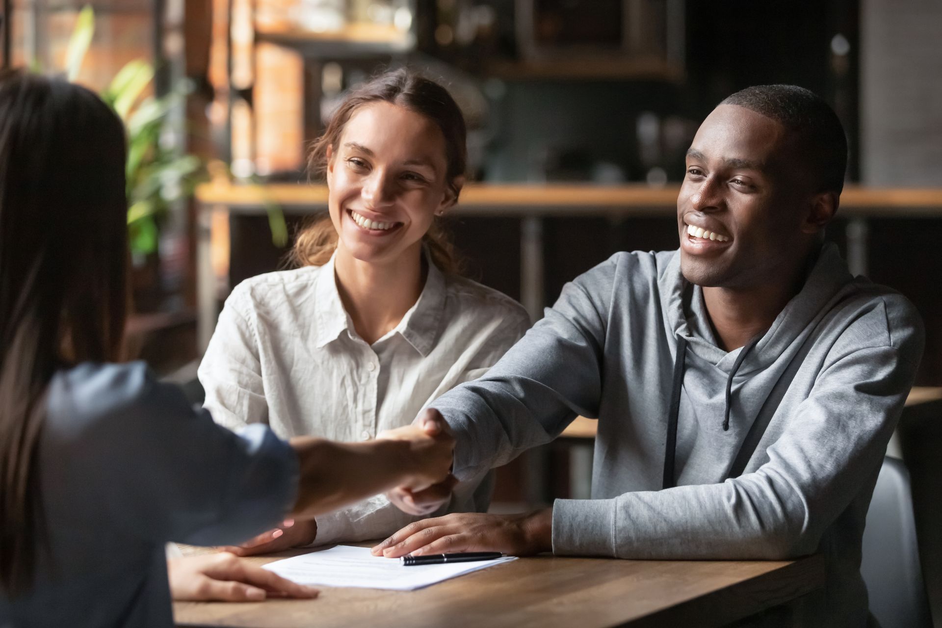 A happy couple shakes hands with a home loan broker to take a mortgage loan.