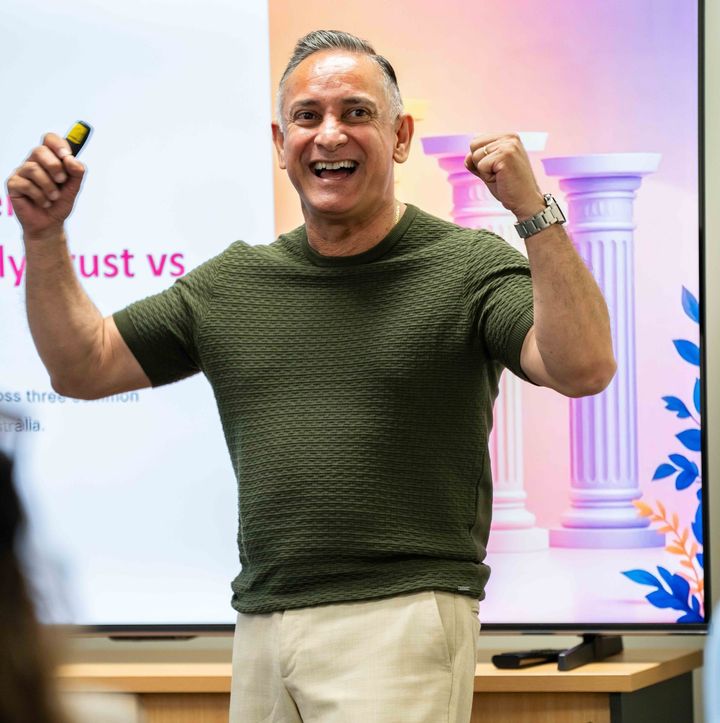 Smiling man in green shirt holding a clicker and flexing fists in front of a presentation screen