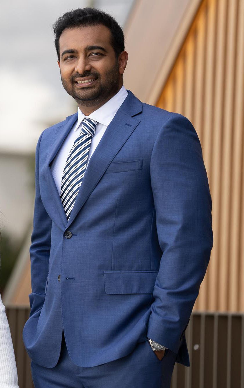 Man in blue suit, smiling, wearing striped tie, posing outside modern building.