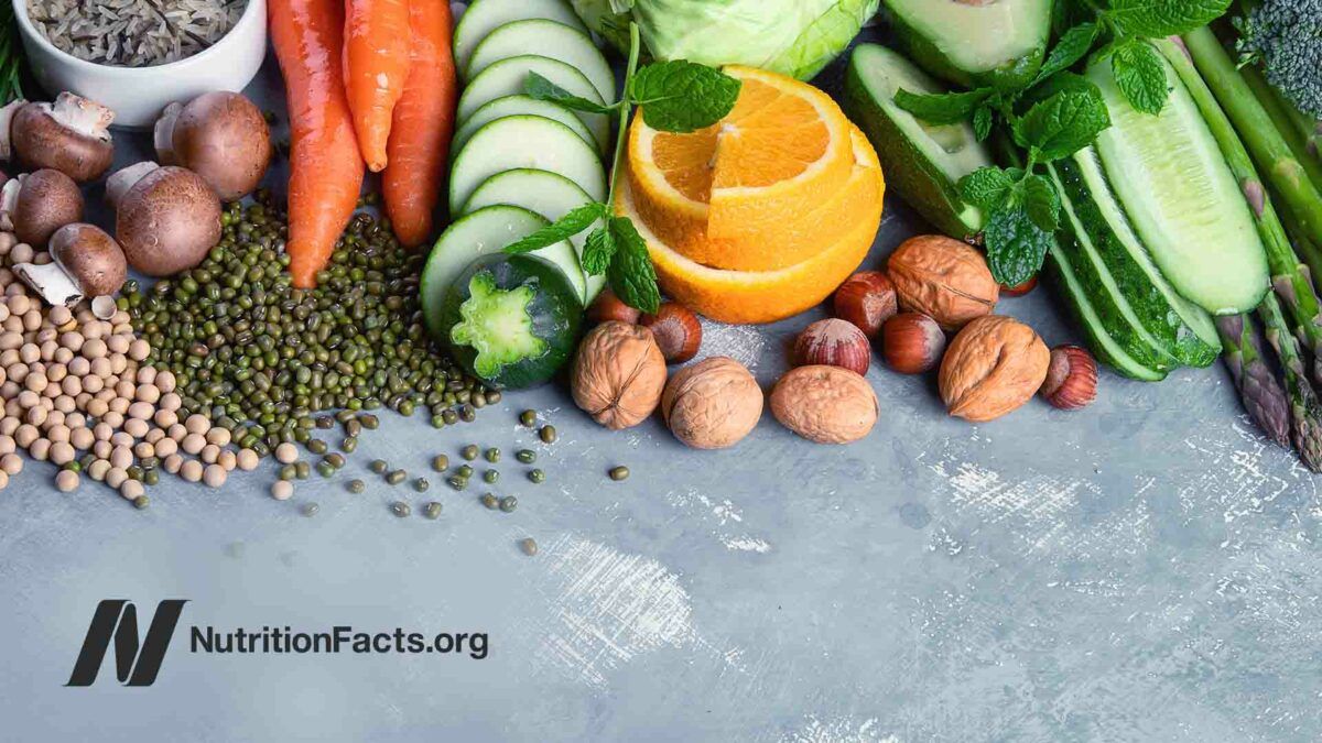 Assortment of fresh vegetables, fruit, nuts, and grains arranged on a gray surface.