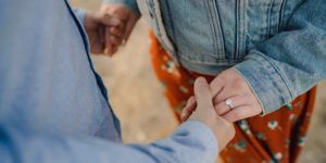 Couple holding hands, showing a ring on the person wearing a jean jacket.