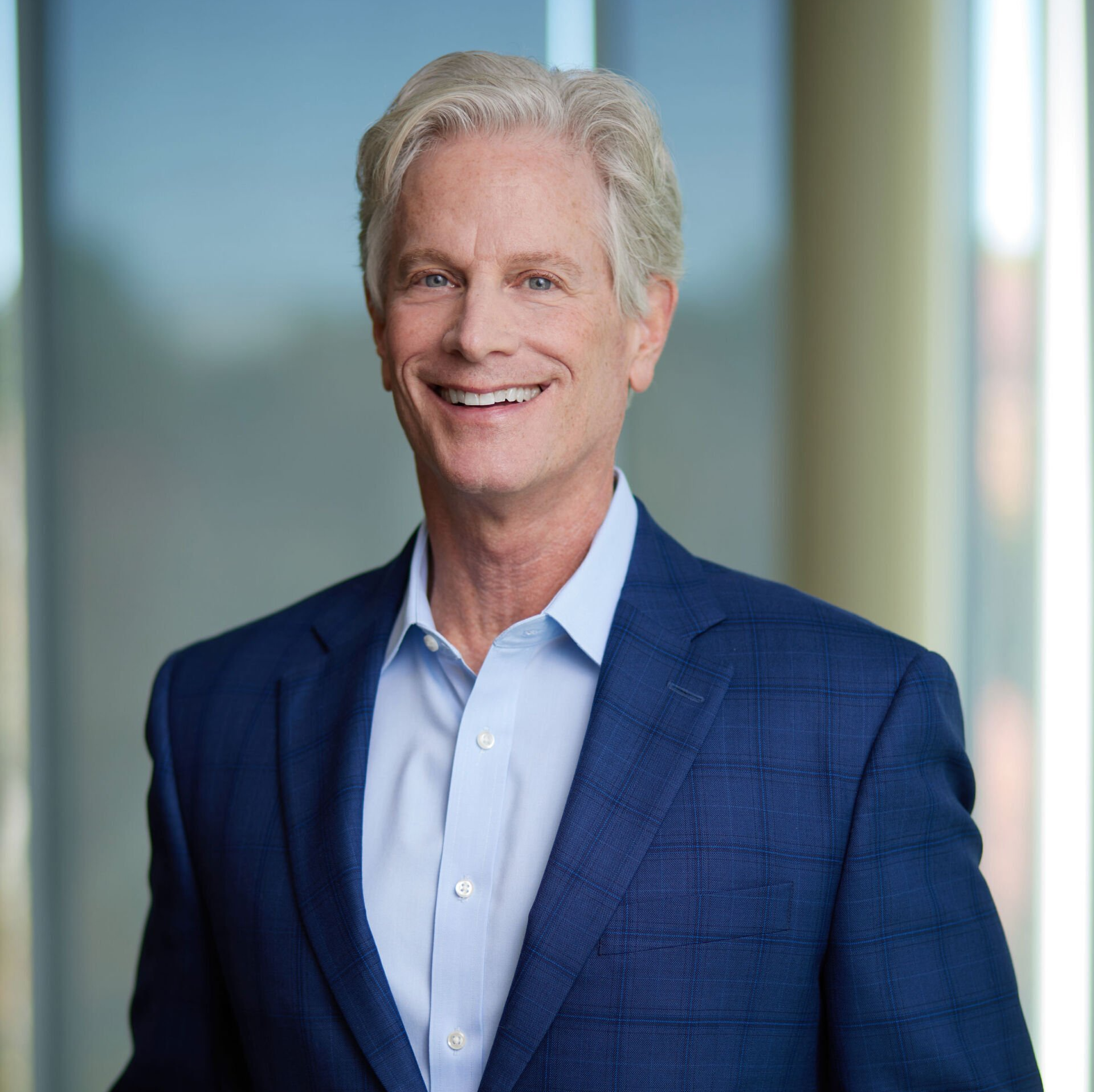 Smiling man with silver hair in a blue suit and open-collared shirt.