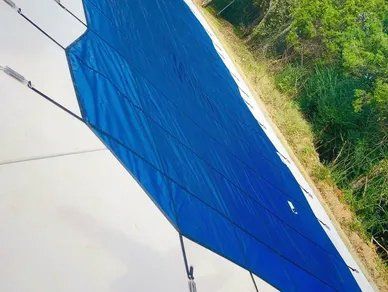 A blue tarp is covering a swimming pool with trees in the background.