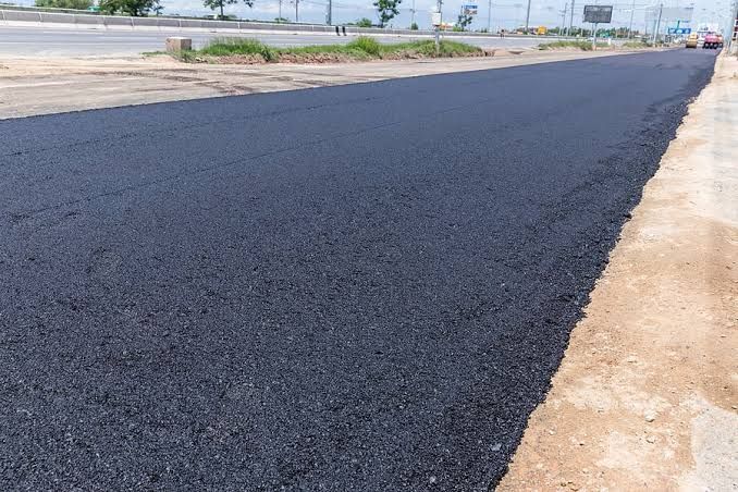 Road workers paving a highway with an orange road roller and fresh black asphalt