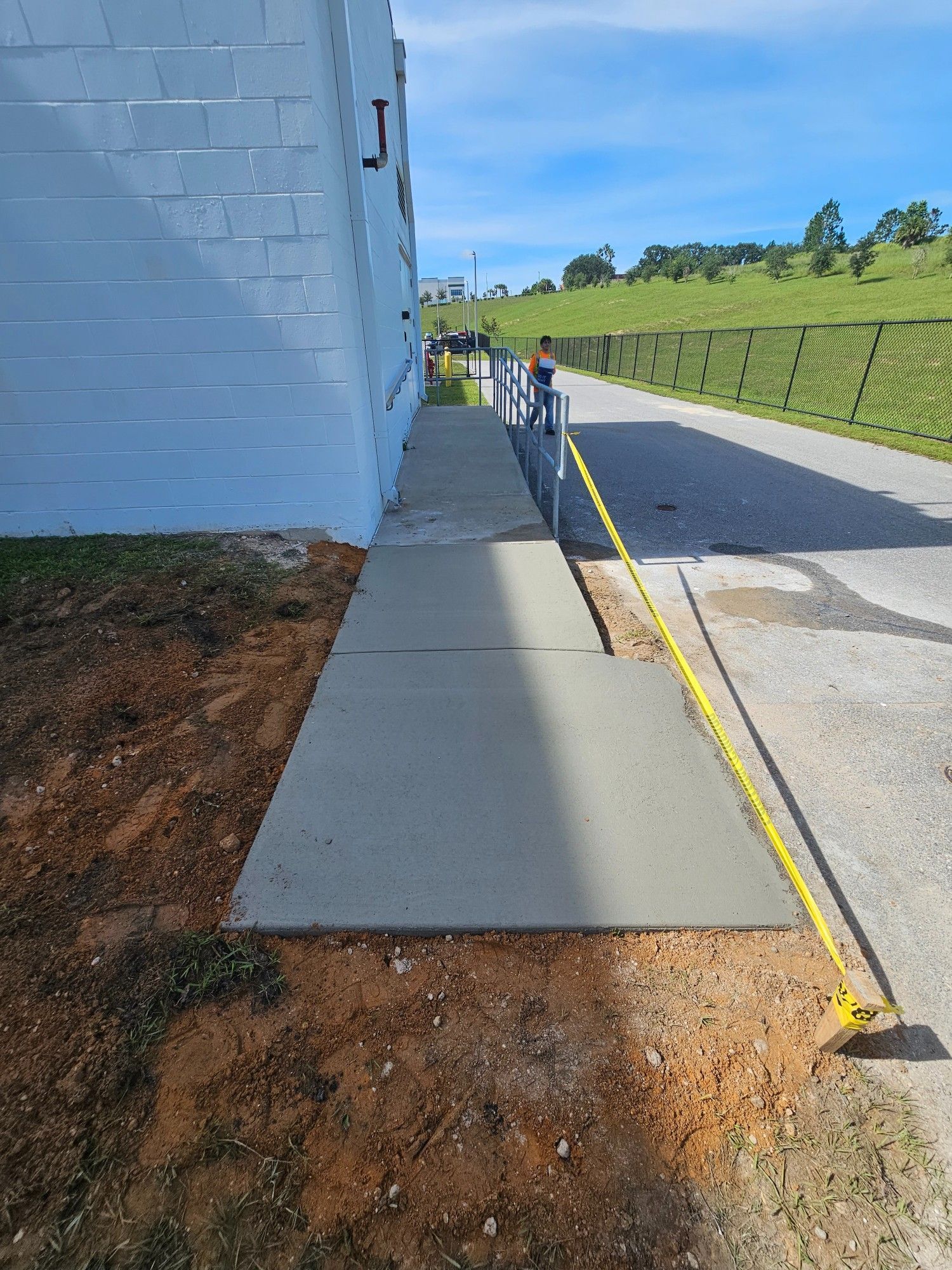 Newly poured concrete walkway next to white building. Yellow caution tape blocks access.