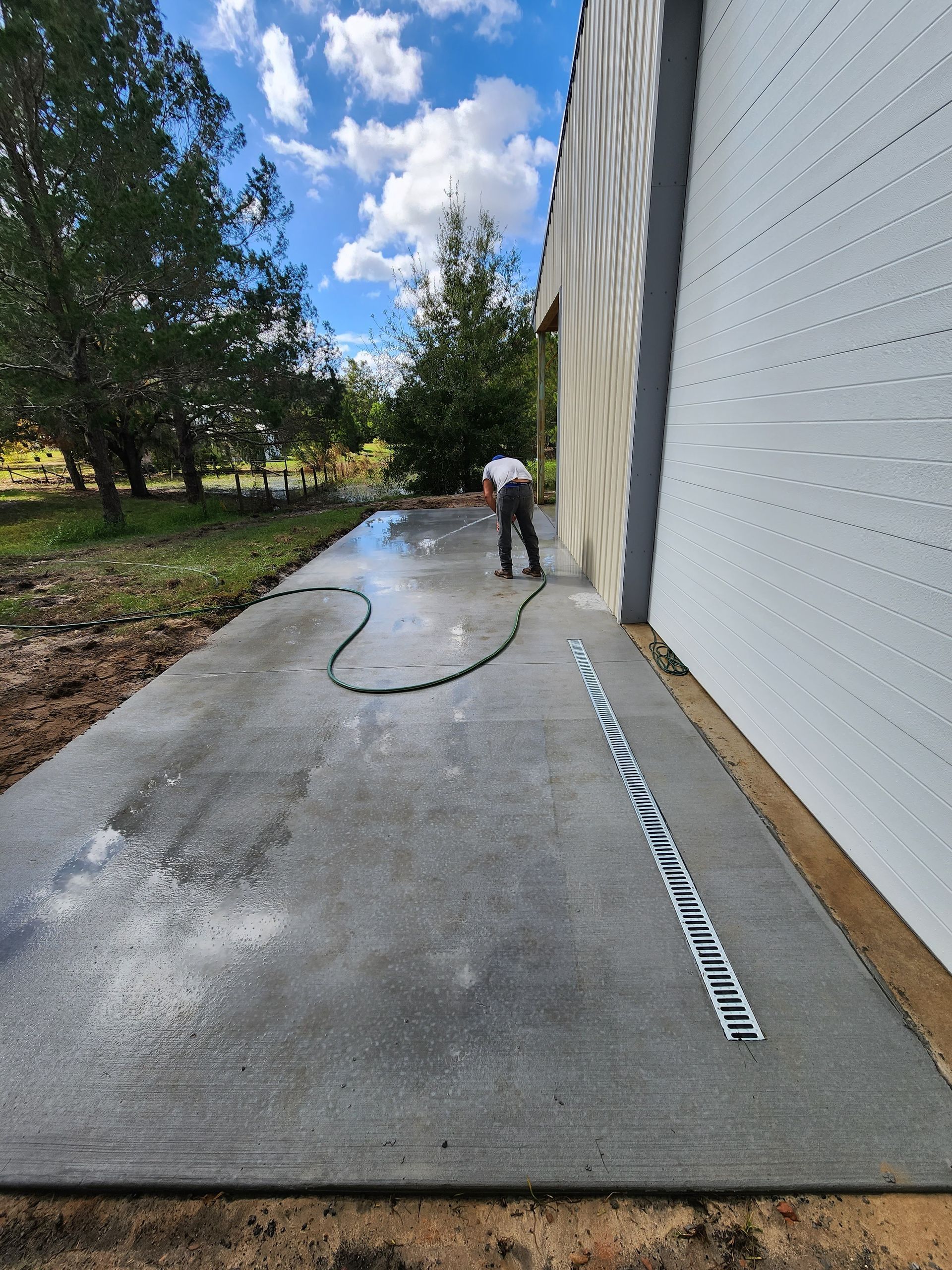 A man is cleaning a concrete driveway with a hose