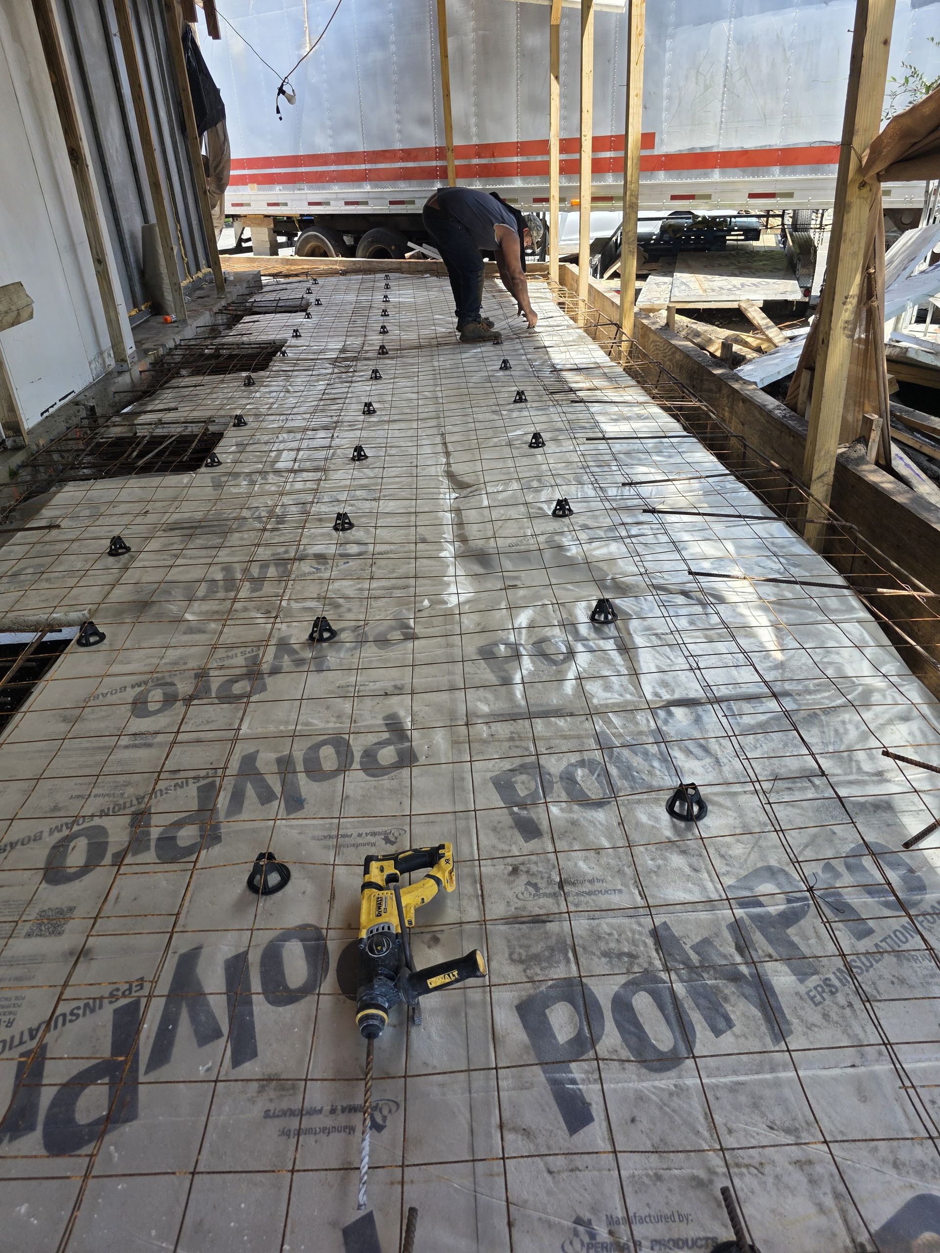 A person working on a construction site. A layer of PolyPro is on the floor, with a drill and plastic brackets.