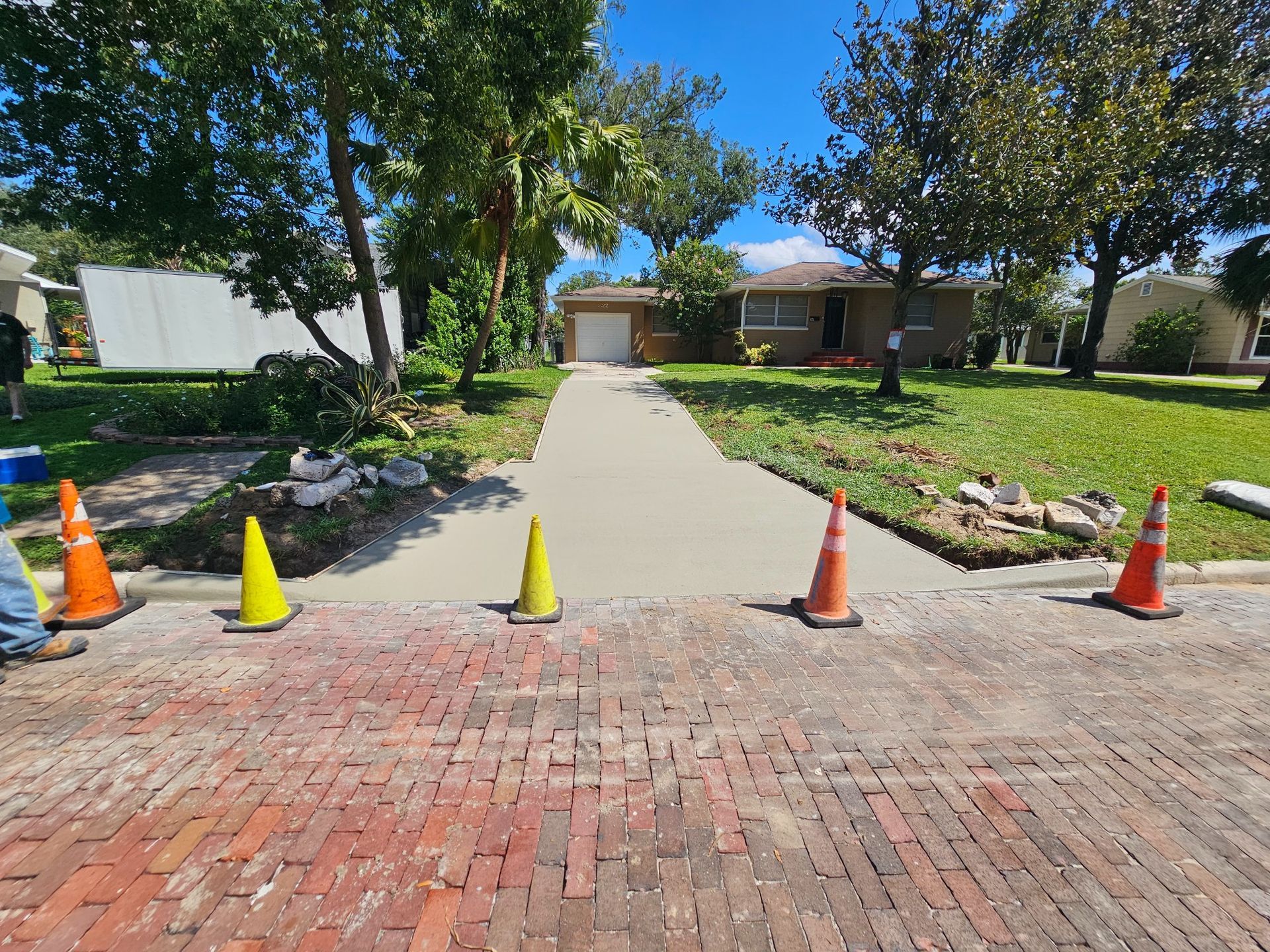 Freshly poured concrete driveway in front of a single-story home. Orange and yellow cones block entry.